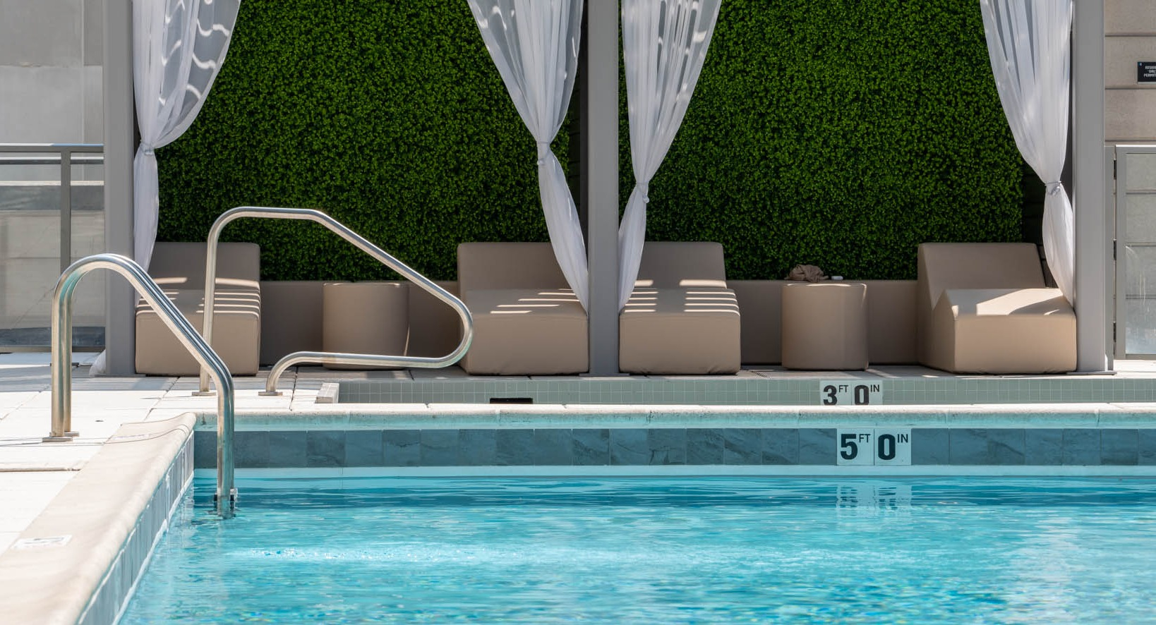 Luxurious poolside area with private cabanas featuring elegant white drapes and lush greenery at K2 Apartments in Chicago