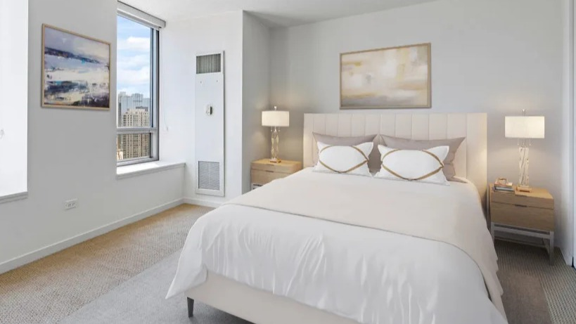 Serene bedroom with a queen-sized bed, soft lighting, and large windows showcasing the urban cityscape at Kingsbury Plaza in Chicago