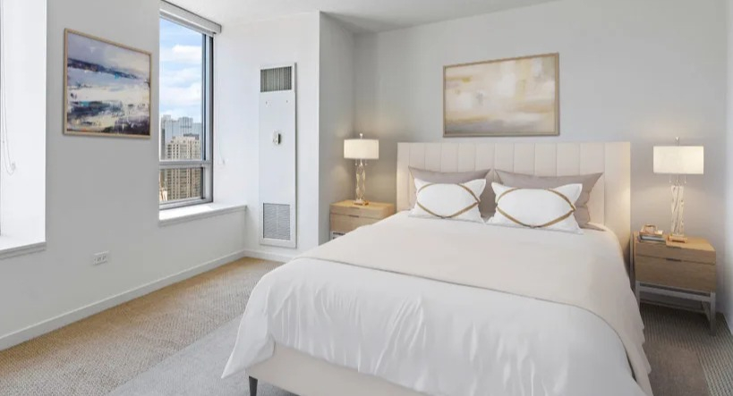Serene bedroom with a queen-sized bed, soft lighting, and large windows showcasing the urban cityscape at Kingsbury Plaza in Chicago