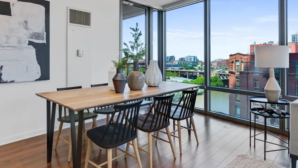 Modern dining and living room with a large table, comfortable seating, and expansive windows offering river views at Kingsbury Plaza in Chicago