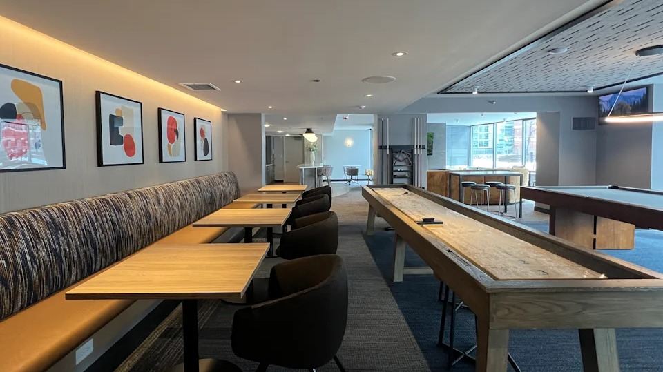 Kingsbury Plaza game room with shuffleboard table, banquet seating, and modern art for resident entertainment