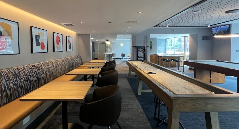 Kingsbury Plaza game room with shuffleboard table, banquet seating, and modern art for resident entertainment