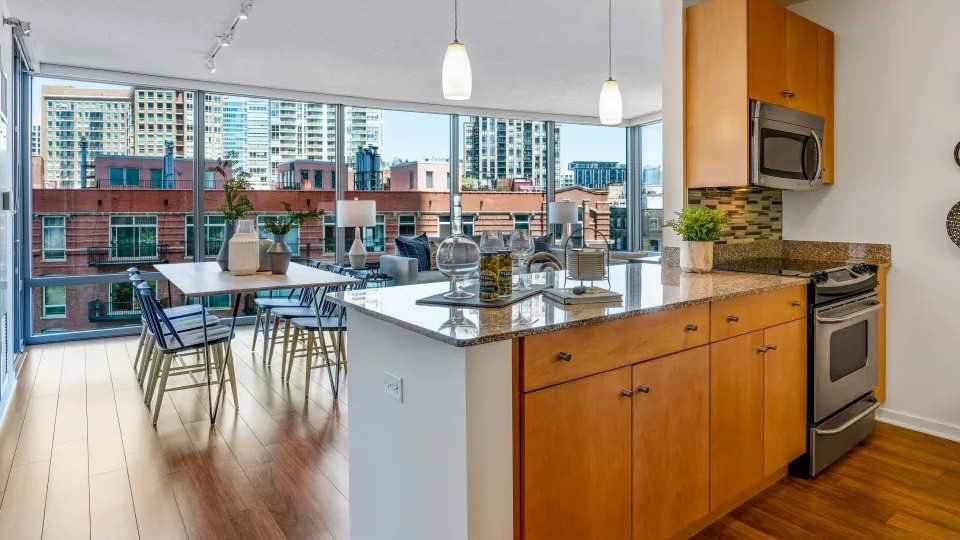 Open-concept kitchen and dining area with granite countertops, wooden cabinetry, and large windows offering city views at Kingsbury Plaza in Chicago