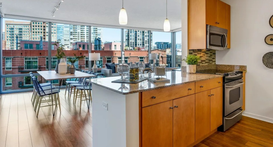 Open-concept kitchen and dining area with granite countertops, wooden cabinetry, and large windows offering city views at Kingsbury Plaza in Chicago