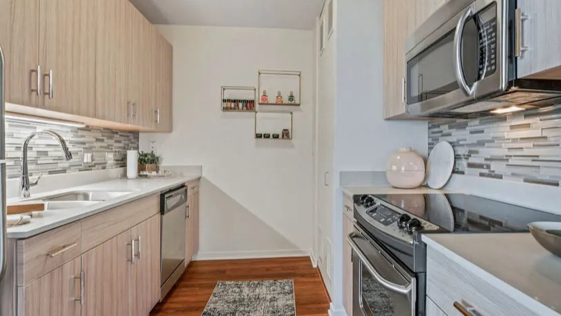 Modern galley kitchen with light wood cabinetry, stainless steel appliances, and a stylish tiled backsplash at Kingsbury Plaza in Chicago