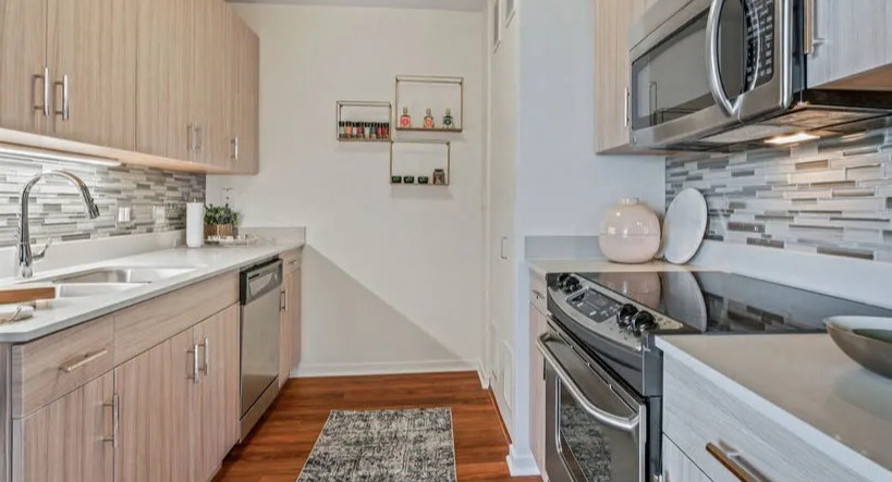 Modern galley kitchen with light wood cabinetry, stainless steel appliances, and a stylish tiled backsplash at Kingsbury Plaza in Chicago