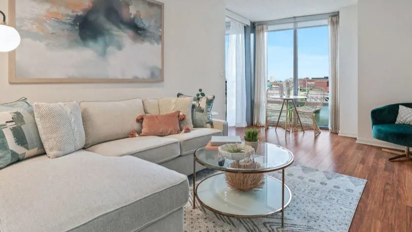 Cozy living room with a large sectional sofa, elegant coffee table, and large windows leading to a balcony at Kingsbury Plaza in Chicago