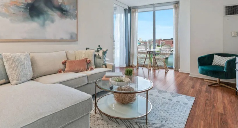 Cozy living room with a large sectional sofa, elegant coffee table, and large windows leading to a balcony at Kingsbury Plaza in Chicago