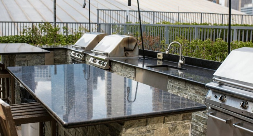 Modern outdoor grilling station with multiple gas grills, granite countertops, and bar seating for residents at Kingsbury Plaza in Chicago