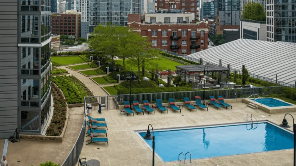 Panoramic view of the Kingsbury Plaza pool area with lounge chairs, a hot tub, and landscaped greenery amidst city buildings in Chicago