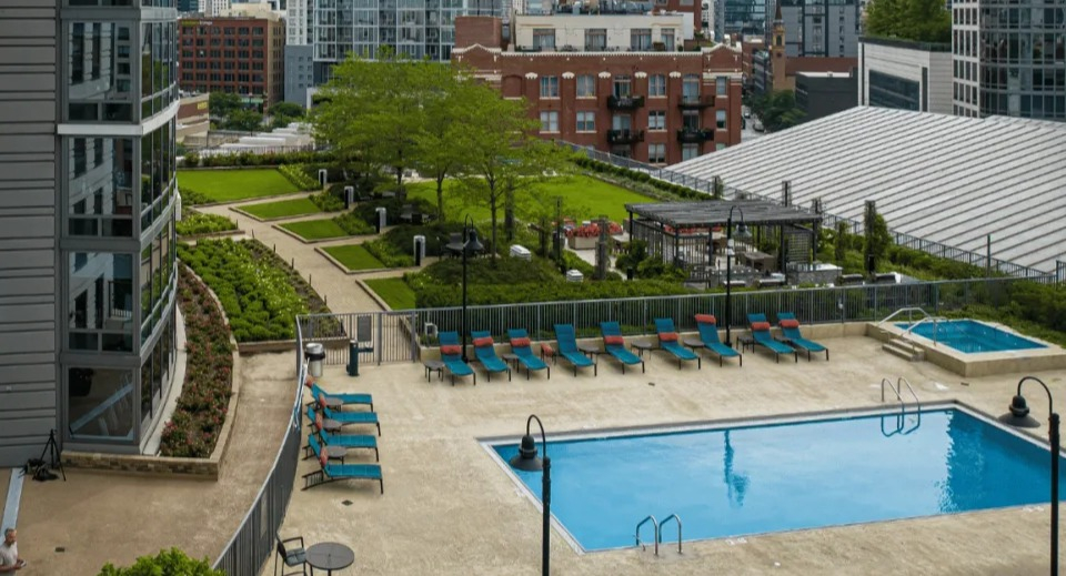 Panoramic view of the Kingsbury Plaza pool area with lounge chairs, a hot tub, and landscaped greenery amidst city buildings in Chicago