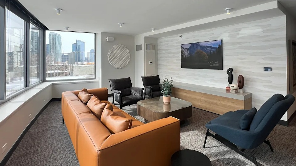 Kingsbury Plaza resident living area with comfortable sofas, a large TV, and expansive windows showcasing city views