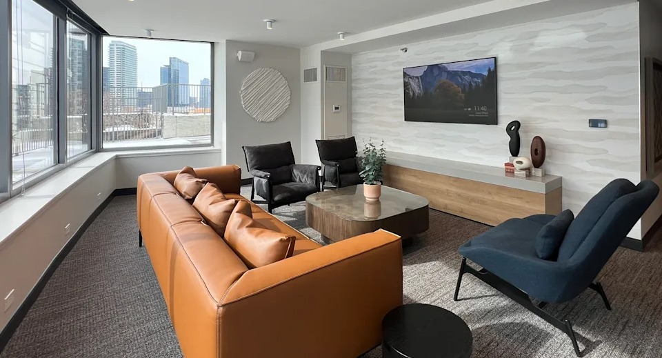 Kingsbury Plaza resident living area with comfortable sofas, a large TV, and expansive windows showcasing city views