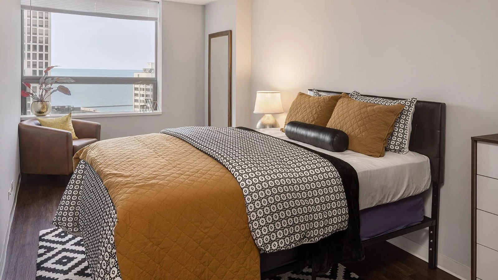 Inviting apartment bedroom at Lake Shore Plaza in Chicago, featuring a comfortable bed, modern dresser, and stunning lake views from the window