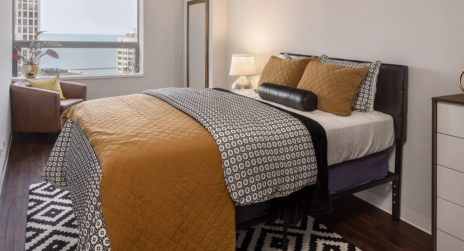 Inviting apartment bedroom at Lake Shore Plaza in Chicago, featuring a comfortable bed, modern dresser, and stunning lake views from the window