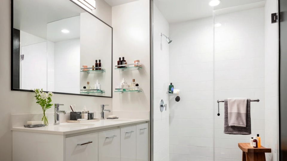 Modern apartment bathroom at Landmark West Loop in Chicago, featuring a double vanity, large mirror, and a glass-enclosed walk-in shower