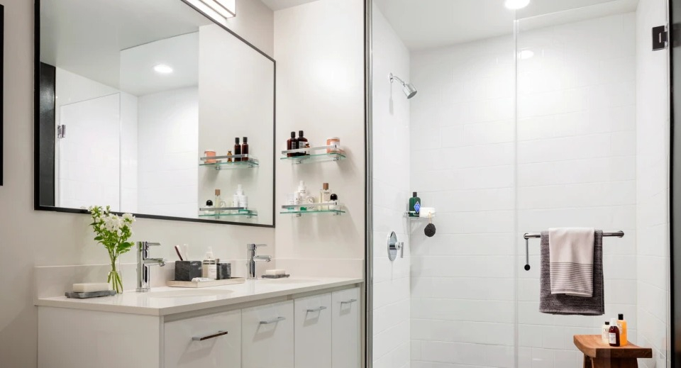 Modern apartment bathroom at Landmark West Loop in Chicago, featuring a double vanity, large mirror, and a glass-enclosed walk-in shower
