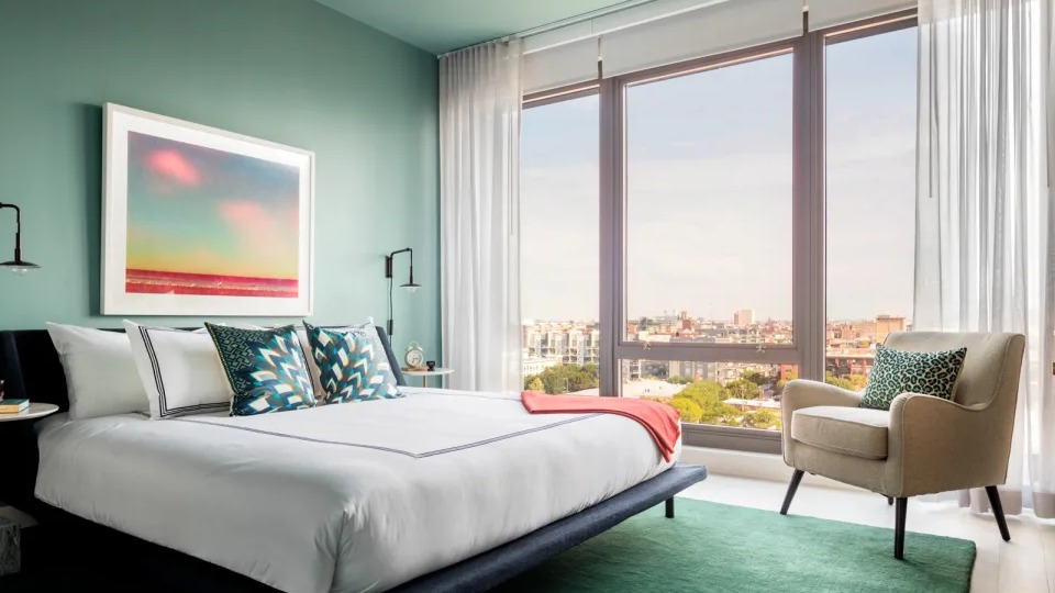 Tranquil apartment bedroom at Landmark West Loop in Chicago, featuring a green accent wall, large bed, and floor-to-ceiling windows with city views