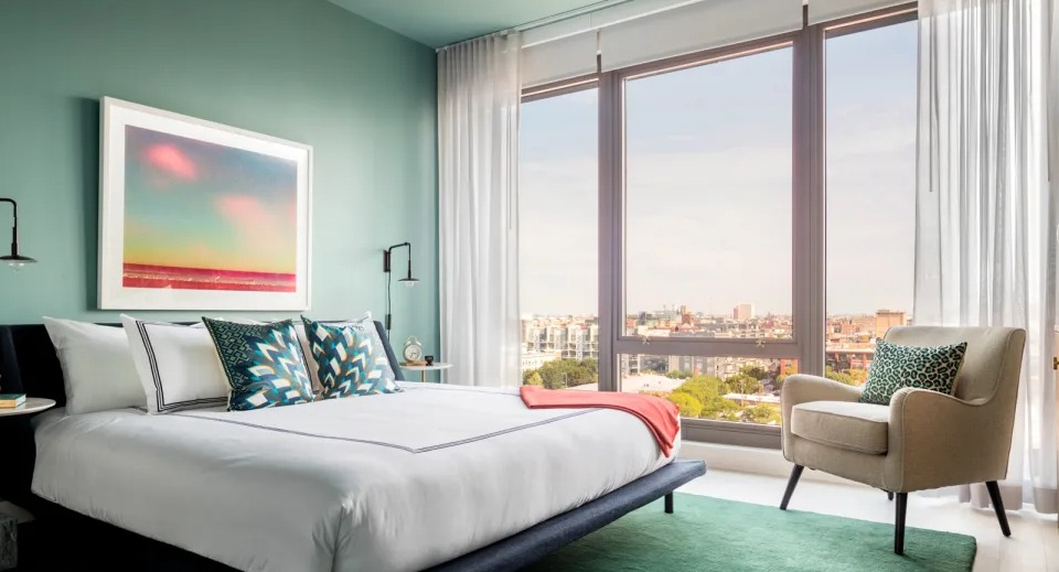 Tranquil apartment bedroom at Landmark West Loop in Chicago, featuring a green accent wall, large bed, and floor-to-ceiling windows with city views