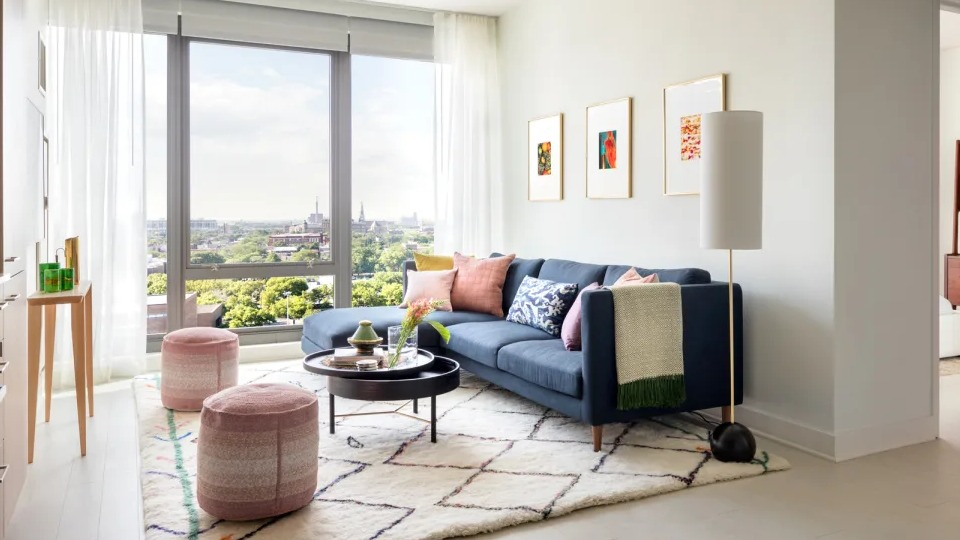 Bright apartment living room at Landmark West Loop in Chicago, featuring a blue sofa, colorful accents, and large windows with city views