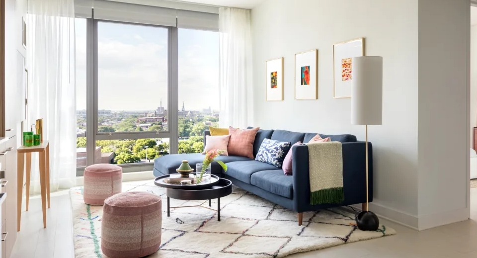 Bright apartment living room at Landmark West Loop in Chicago, featuring a blue sofa, colorful accents, and large windows with city views