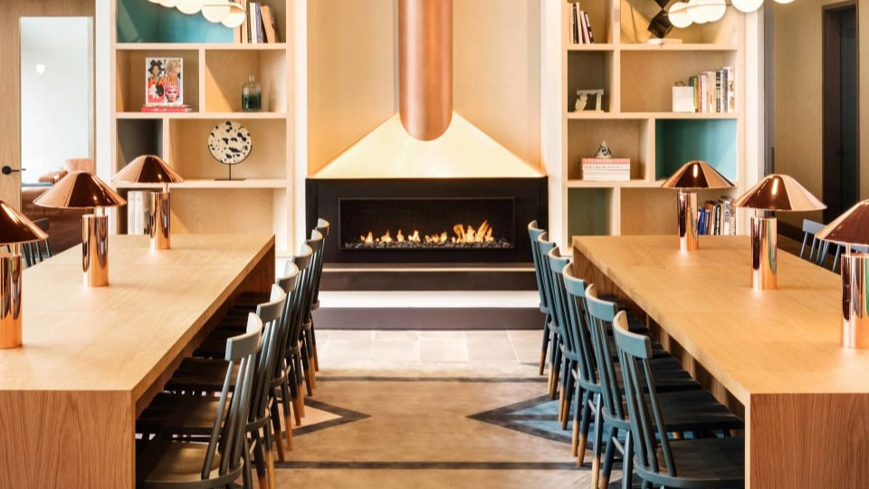 Modern lounge area with a sleek fireplace, shared dining tables, and artistic shelving at Landmark West Loop apartments in Chicago