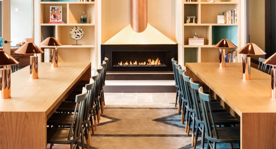 Modern lounge area with a sleek fireplace, shared dining tables, and artistic shelving at Landmark West Loop apartments in Chicago
