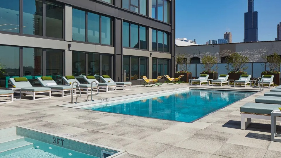 Inviting outdoor pool and hot tub area with sun loungers and city skyline views at Landmark West Loop apartments in Chicago