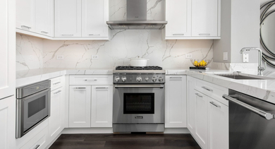 Gourmet kitchen featuring white cabinets, high-end stainless steel appliances, and marble countertops at Left Bank apartments in Chicago