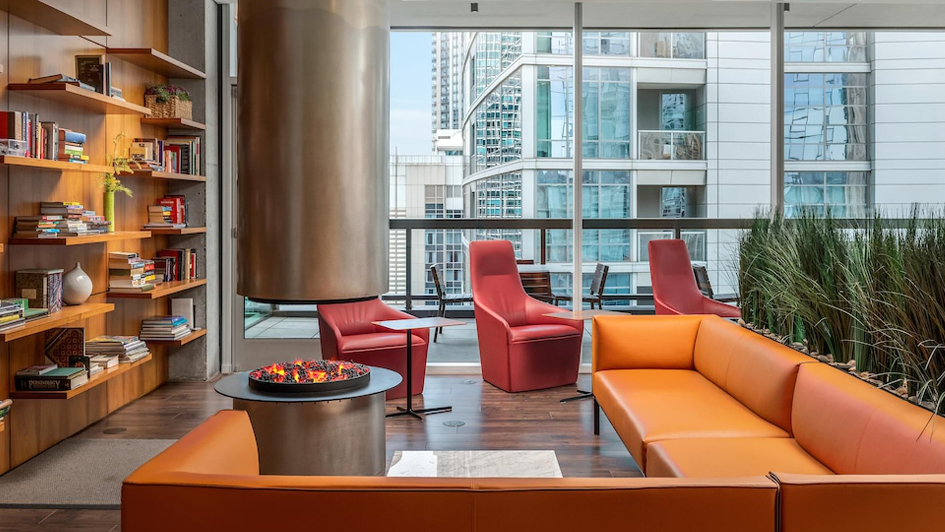 Resident library lounge with built-in bookshelves, cozy orange sofas, and a modern fireplace at Optima Signature apartments in Chicago