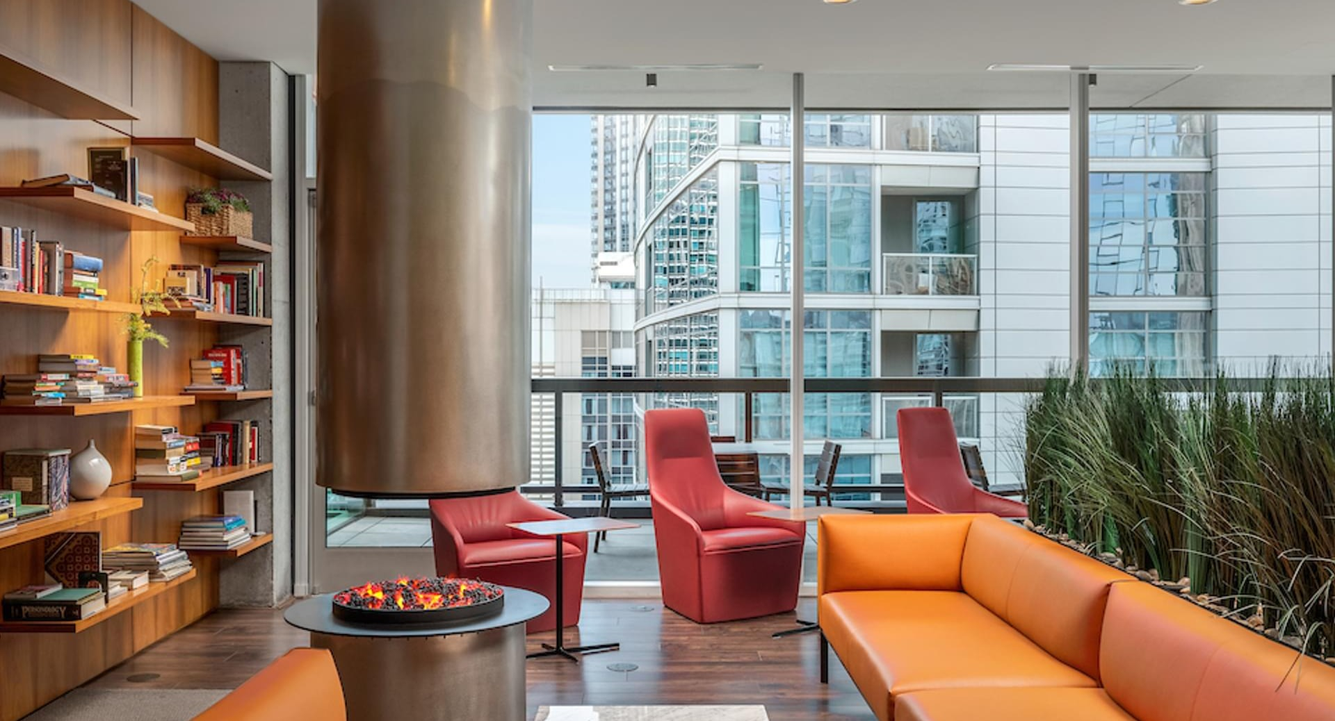 Resident library lounge with built-in bookshelves, cozy orange sofas, and a modern fireplace at Optima Signature apartments in Chicago