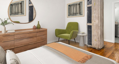 Modern bedroom at The Lofts at Gin Alley in Chicago, featuring a comfortable bed, wooden dresser, and an industrial exposed pillar