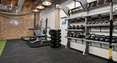 Industrial-chic gym at The Lofts at Gin Alley in Chicago, featuring kettlebells, free weights, and exposed brick