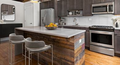 Modern industrial kitchen at The Lofts at Gin Alley in Chicago, featuring a large island, stainless steel appliances, and exposed wooden beams