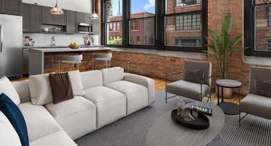 Open-concept living room and kitchen at The Lofts at Gin Alley in Chicago, featuring exposed brick, modern appliances, and a large sofa