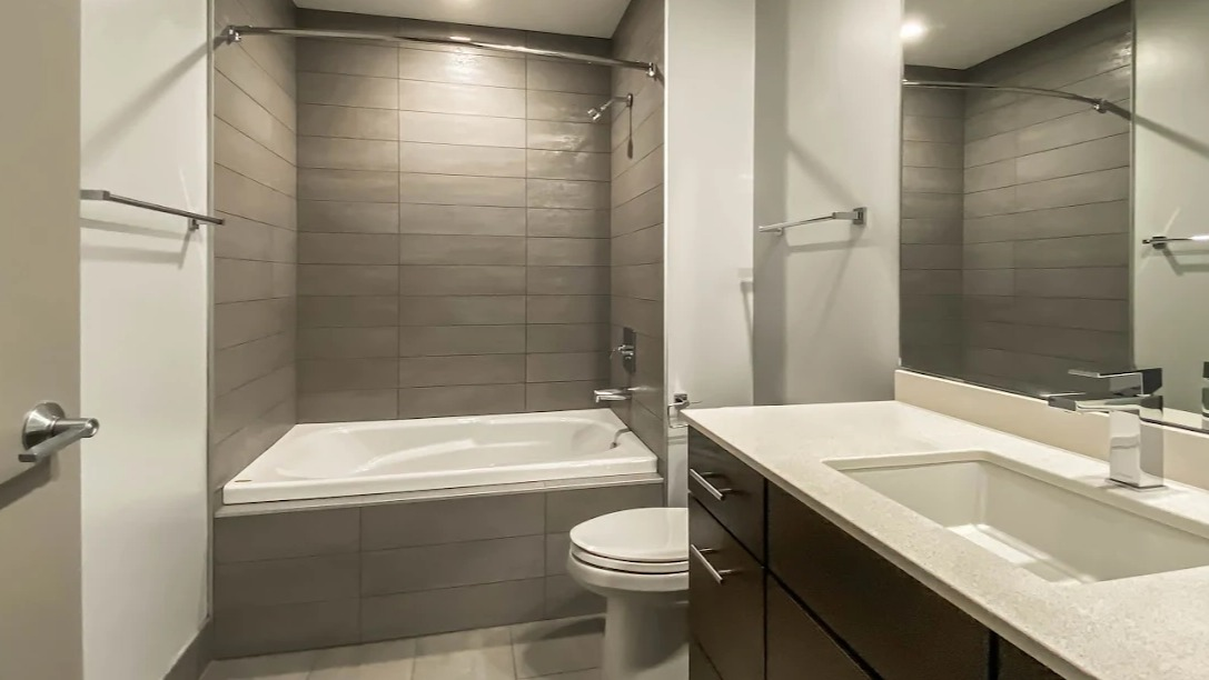 Contemporary bathroom with a spacious vanity, sleek fixtures, and a shower-tub combination with grey tile at Lofts at River East in Chicago