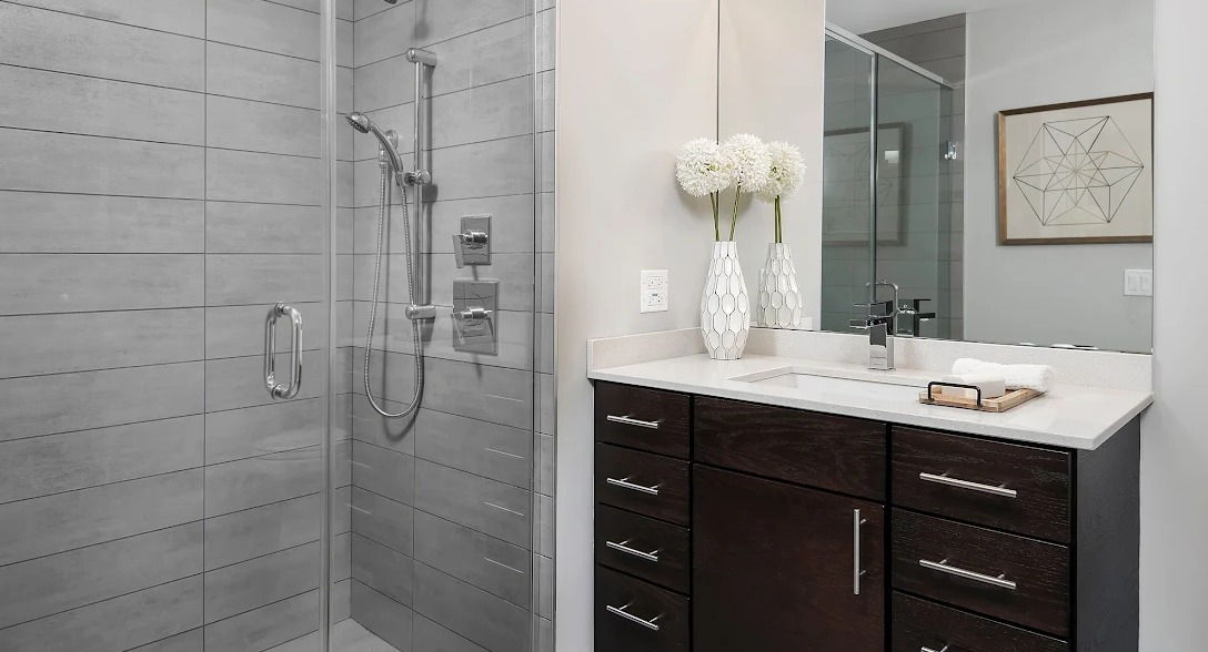 Modern bathroom featuring a spacious walk-in glass shower, single vanity, and contemporary gray tile at Lofts at River East in Chicago