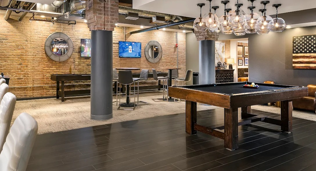 Lively game room featuring a pool table, bar area with seating, arcade games, and exposed brick walls at Lofts at River East in Chicago