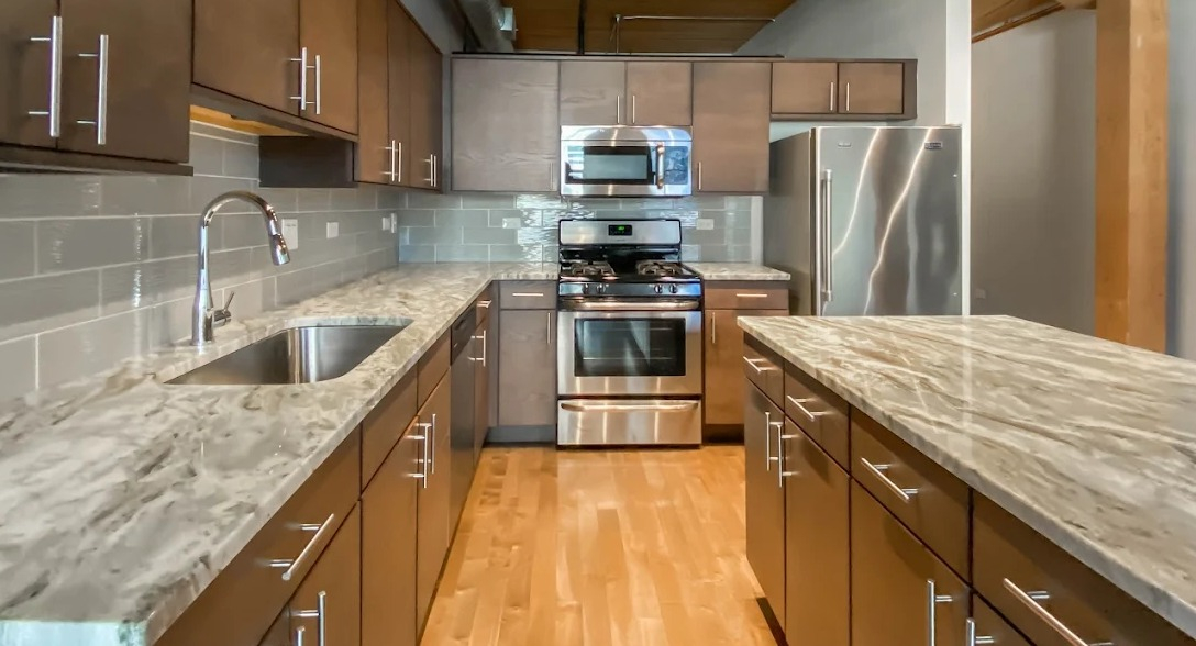 Gourmet kitchen with dark wood cabinets, granite countertops, a large island, stainless steel appliances, and wood ceilings at Lofts at River East in Chicago