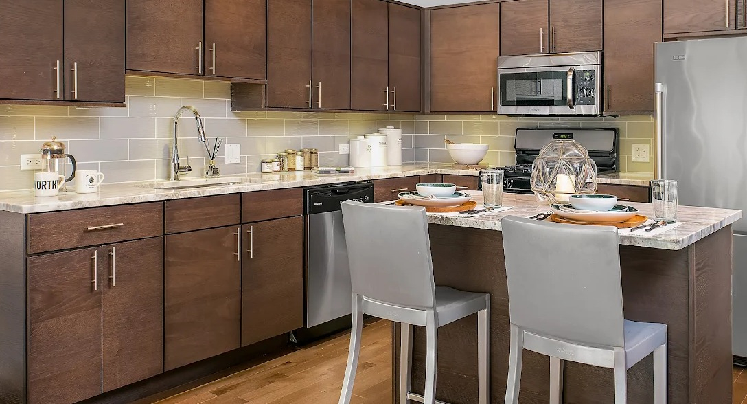 Modern kitchen featuring a large island with bar seating, wood cabinets, stainless steel appliances, and exposed ductwork at Lofts at River East in Chicago