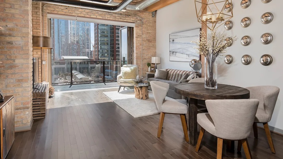 Spacious loft living and dining area with exposed brick, high ceilings, city views, and modern industrial decor at Lofts at River East in Chicago
