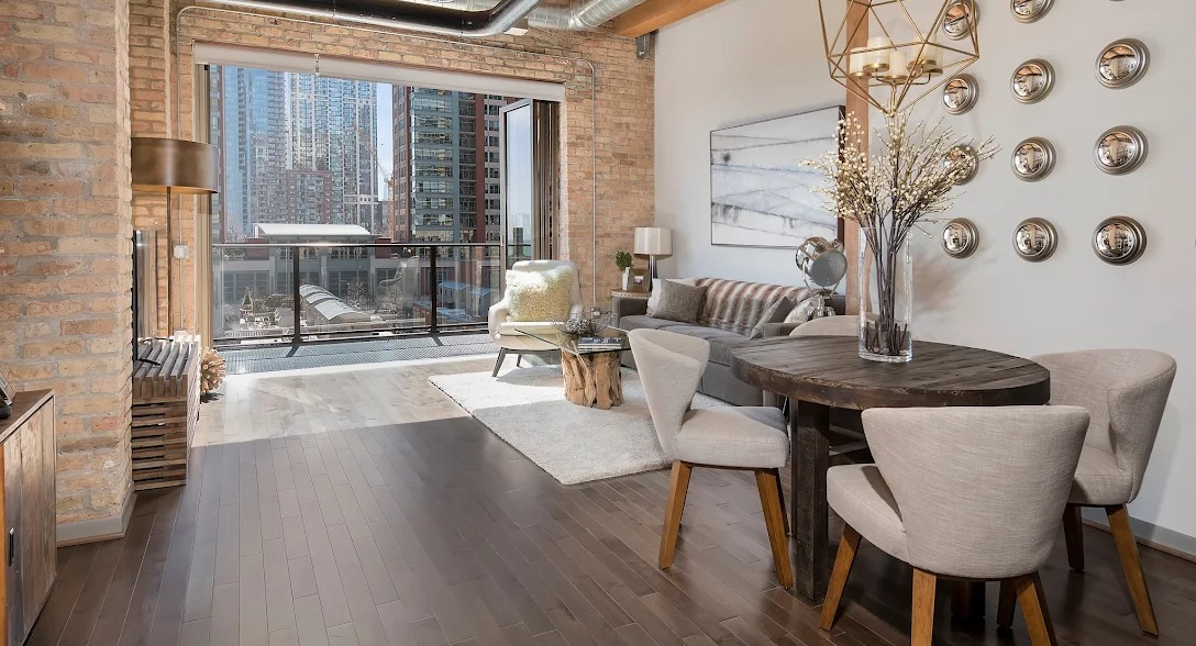 Spacious loft living and dining area with exposed brick, high ceilings, city views, and modern industrial decor at Lofts at River East in Chicago