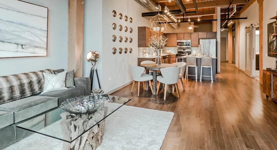 Open-concept living room and kitchen area featuring exposed brick, high wood ceilings, and modern furniture at Lofts at River East in Chicago