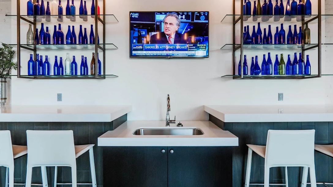 Modern resident bar area with elegant blue glass bottle decor, bar stools, a sink, and a TV for news at Lofts at River East in Chicago