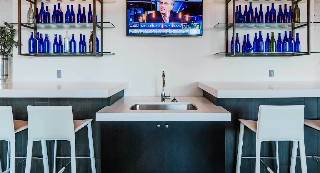 Modern resident bar area with elegant blue glass bottle decor, bar stools, a sink, and a TV for news at Lofts at River East in Chicago