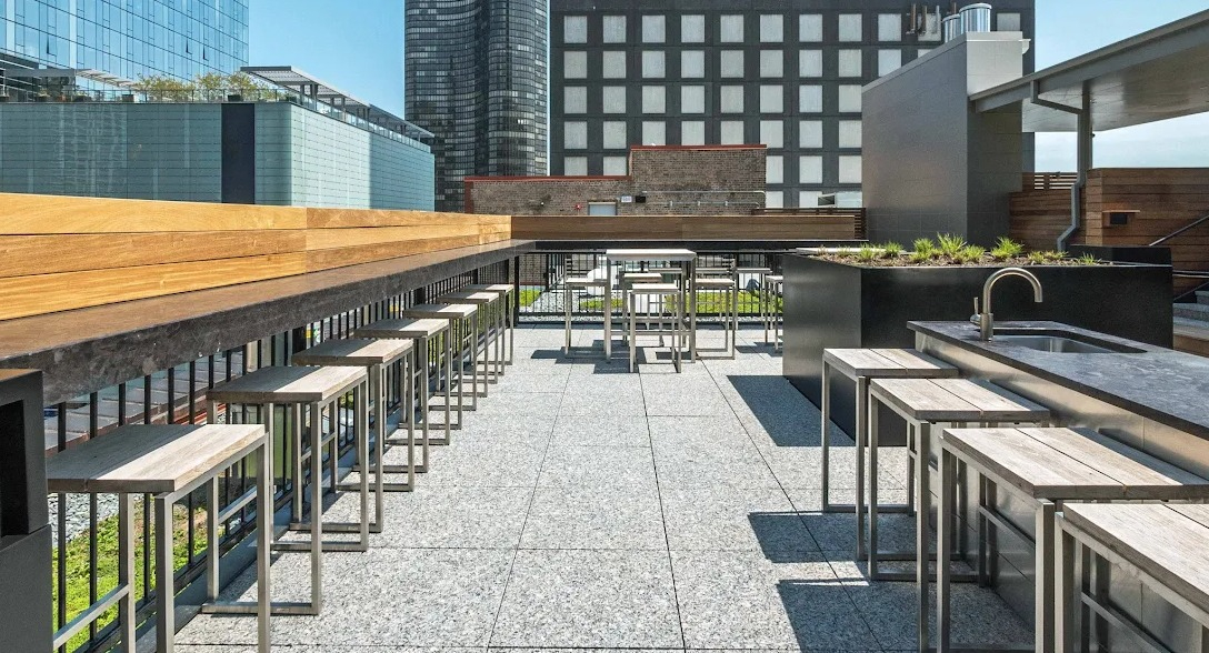 Stylish rooftop bar and grilling area with bar stools, sleek countertops, and panoramic city views at Lofts at River East in Chicago