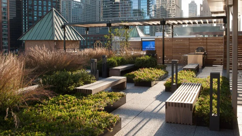 Landscaped rooftop terrace with comfortable benches, lush greenery, and a communal grilling area amidst city buildings at Lofts at River East in Chicago