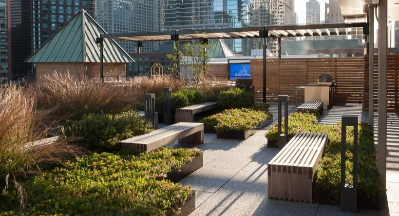 Landscaped rooftop terrace with comfortable benches, lush greenery, and a communal grilling area amidst city buildings at Lofts at River East in Chicago