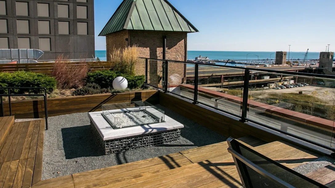 Scenic rooftop patio with a modern fire pit, wooden decking, and expansive views of the river and city skyline at Lofts at River East in Chicago