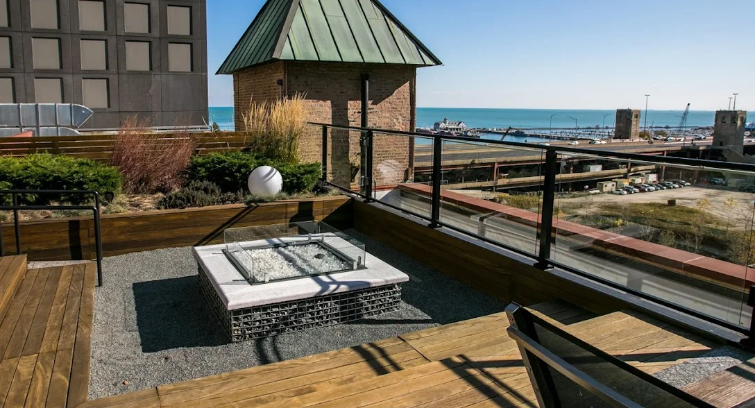 Scenic rooftop patio with a modern fire pit, wooden decking, and expansive views of the river and city skyline at Lofts at River East in Chicago
